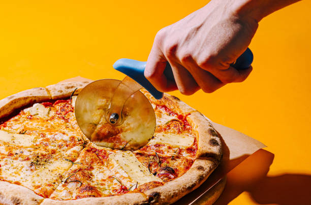 istock Hand slicing a fresh pizza with a pizza cutter on a vibrant yellow background 2202034973