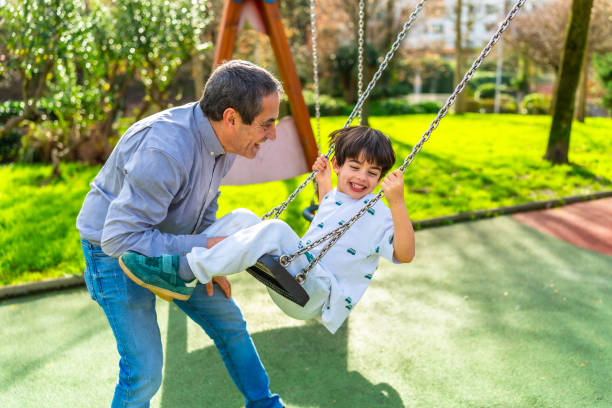 istock Grandfather pushing grandson on swing in playground 2202036431