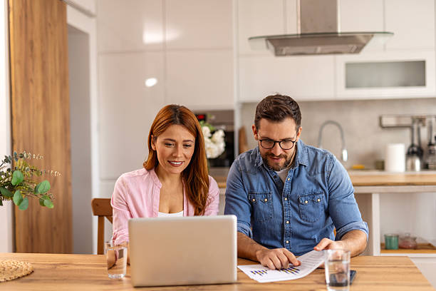 istock Couple is sitting at a table, focused on a laptop screen. They be discussing or working together, highlighting themes of collaboration, technology, and modern lifestyle in a home office setting 2202036917