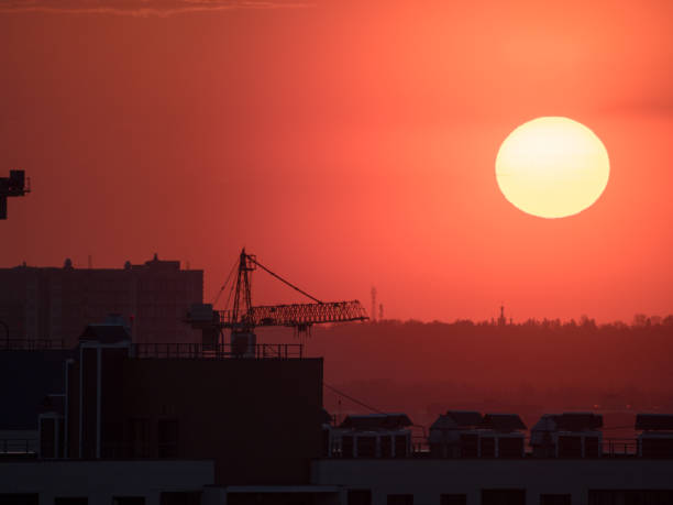 sunset with bright sun over city and construction site with cranes