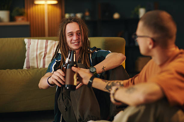 Two friends sitting on floor, sharing a cheerful moment with drinks in cozy living room, illuminated with warm light, expressing happiness and camaraderie