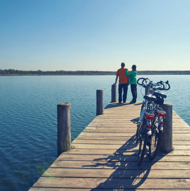 active mature couple standing on wooden pier with their bicycles