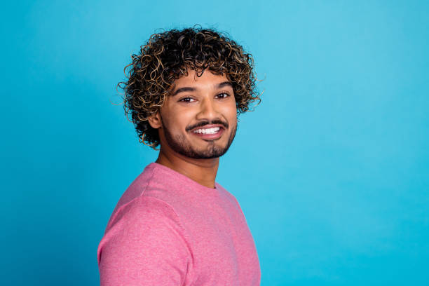 istock Smiling young stylish man wearing a pink pullover posing confidently against a vibrant blue background 2202047671