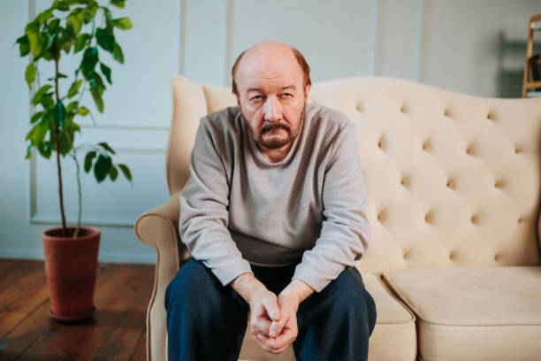 Older man sitting on a sofa with a contemplative expression indoors