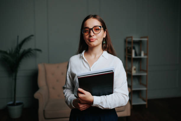 Young woman with glasses holding folders in a cozy indoor setting