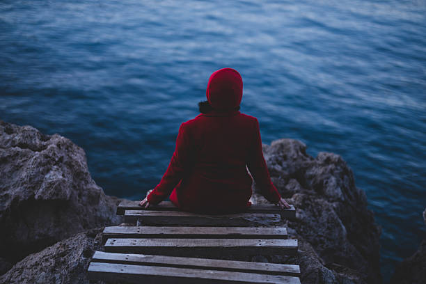 Woman in red coat watching the sea from the wooden pier on the rocks