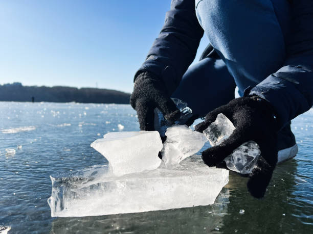 istock Person handling clear ice pieces on a frozen lake under sunlight 2202052286