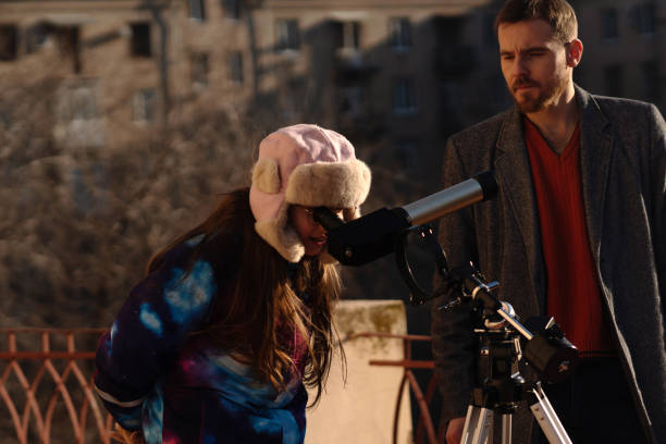 Girl and instructor use tripod-mounted telescope for rooftop solar study. Education, teaching, learning concept