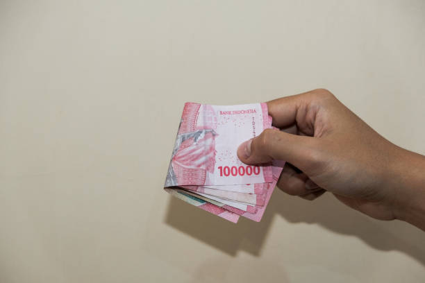 istock A man hand Holding hundred thousand rupiah cream background 2202055437