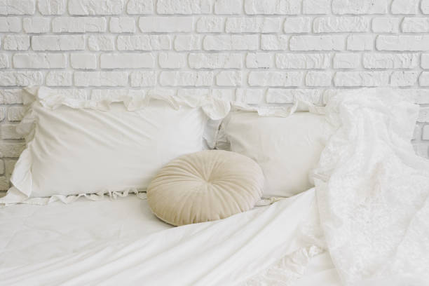 istock Cozy and inviting white bedding, stylish minimalist bed with pillows in white brick wall background 2202058450