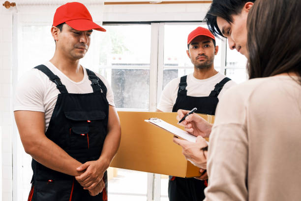 istock Two professional delivery workers in uniforms and red caps deliver a package to customers at home. A couple signs a clipboard, confirming receipt, symbolizing logistics, shipping, and e-commerce. 2202059285