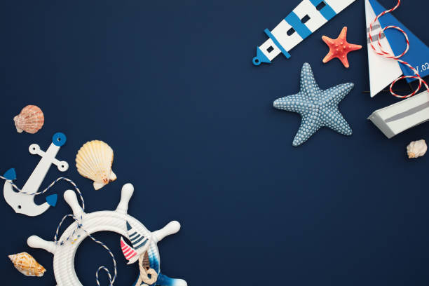 istock Nautical flat lay composition with seashells, starfish, anchor, ship wheel, lighthouse, and toy sailboat on a dark blue background 2202059920