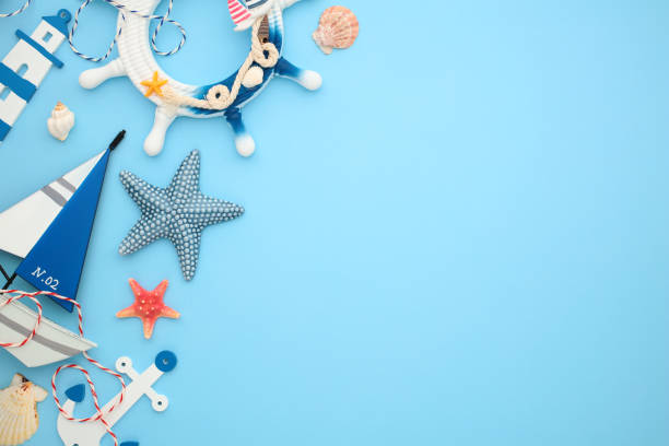 istock Flat lay composition with nautical design elements, sailboat, anchor, steering wheel, lighthouse, seashells, and starfish on light blue background, 2202059932
