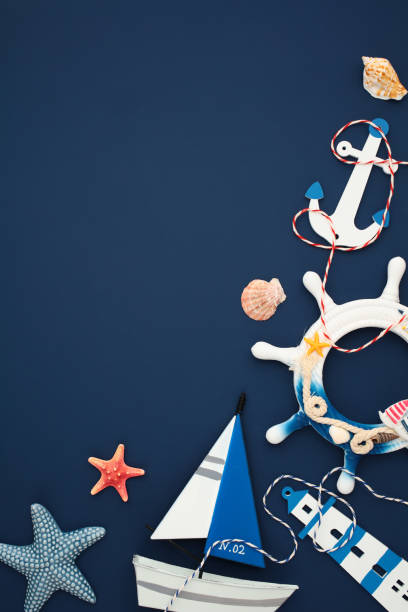 istock Marine flat lay featuring anchor, seashells, ship wheel, starfish, sailboat, and lighthouse decorations on navy blue background 2202059947