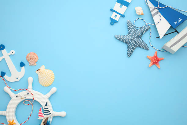 istock Nautical concept with sailboat, anchor, steering wheel, lighthouse, seashells, and starfish on light blue background. Flat lay, top view, copy space 2202059968