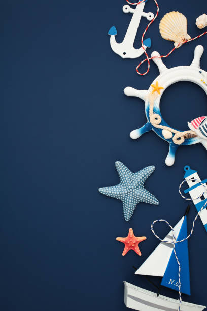 istock Nautical flat lay with anchor, starfish, seashells, lighthouse, and sailboat on a navy blue background 2202060038