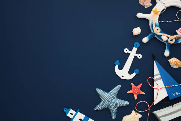 istock Nautical flat lay composition with marine elements on a dark blue background. Top view sailboat, anchor, steering wheel, lighthouse, seashells, and starfish. 2202060101