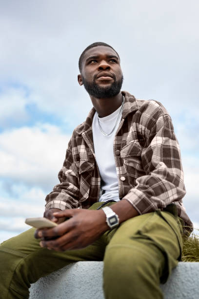 istock Young African man with phone sitting on a wall outdoors 2202070119