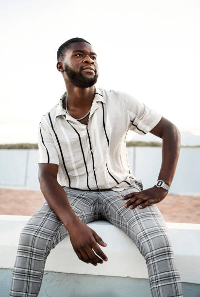 istock Handsome African man sitting on wall outdoors looking away 2202070194