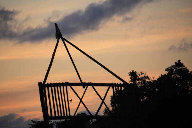 A bamboo scout gate stands silhouetted against a colorful sunset sky, reflecting adventure, skills, and the spirit of scouting.