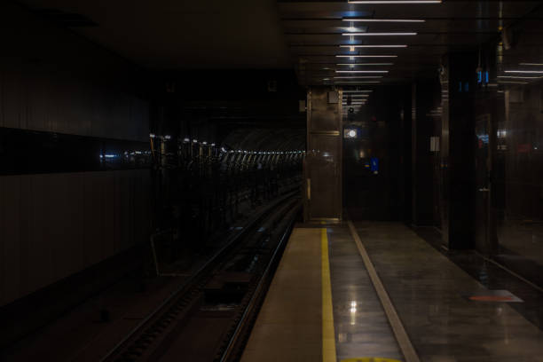 A dimly lit empty subway or metro station platform with the tracks disappearing into a dark tunnel, creating an atmosphere of waiting for a train to arrive. Empty underground metro station..