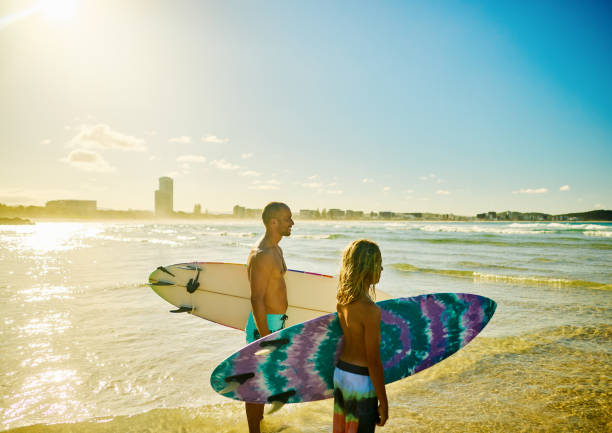 istock Father and son carrying surfboards on sunny Australian beach 2202074254