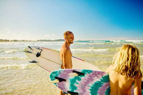 Father and son carrying surfboards, enjoying summer vacation on a sunny Australian beach
