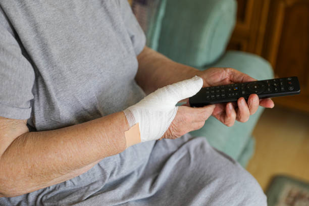 Elderly Woman Caring for a Thumb Injury While Holding a Remote