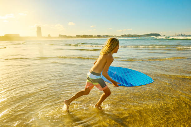 A sun-soaked day unfolds at Bondi Beach as a young man carries his surfboard, embodying the vibrant spirit of outdoor recreation and healthy living. Waves crash nearby, enhancing the fun atmosphere.