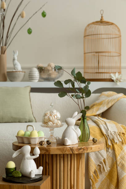 istock Spring composition of living room interior with round coffee table, beige sofa, easter bunny sculpture, colorful easter eggs,  yellow plaid, meringues and personal accessories. Home decor. Template. 2202074509