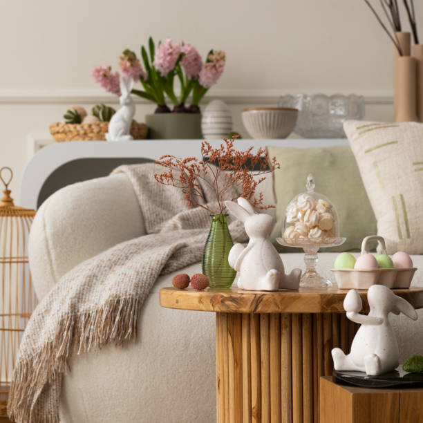 Warm and cozy composition of easter living room interior with coffee table, white sofa, colorful easter eggs, easter bunny, hyacinth, vase with branch and personal accessories. Home decor. Template.