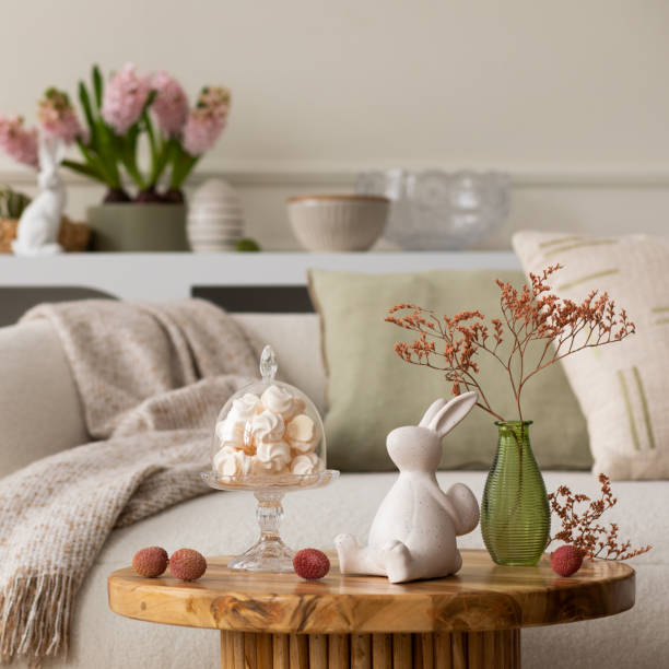 istock Warm and cozy composition of easter living room interior with coffee table, white sofa, colorful easter eggs, easter bunny, hyacinth, vase with branch and personal accessories. Home decor. Template. 2202074669