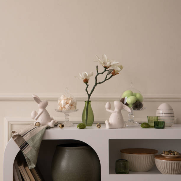 istock Minimalist composition of easter living room interior with copy space, easter bunny sculpture, easter eggs, vase with magnolia, wall with stucco and personal accessories. Home decor. Template. 2202074692