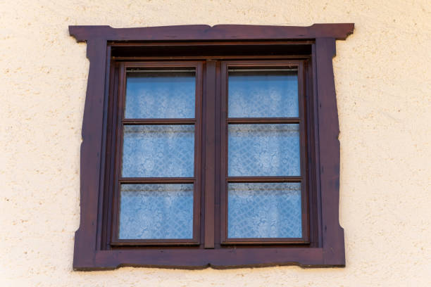 istock Antique wooden window with carved frame - classic window with openwork curtains against a warm textured wall. 2202081757