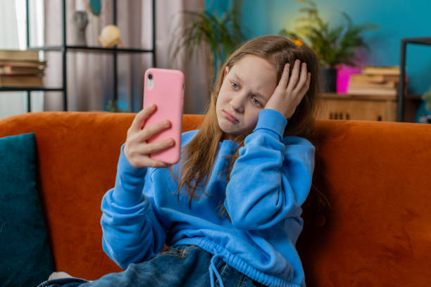 istock Upset child kid girl using smartphone playing game loses bad news fail education study test at home 2202084470