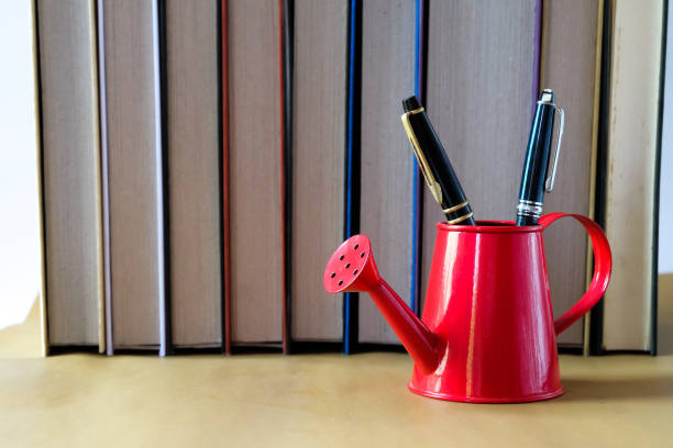 istock Red waterring cans on table with books background. 2202089726