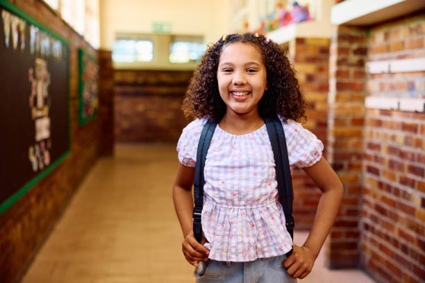 istock School girl in corridor carrying backpack and wearing gingham blouse, smiling at camera 2202091717
