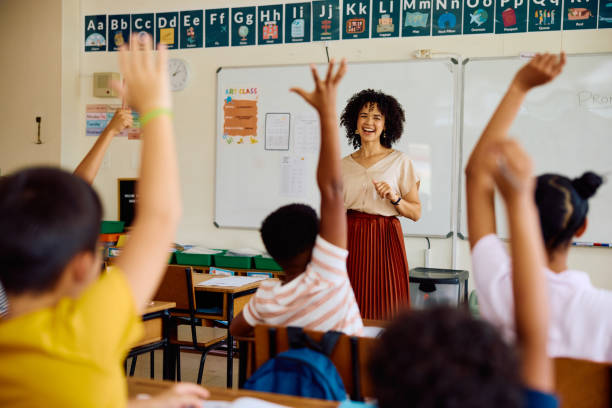 School children sitting at desks with arms up to answer question, enthusiasm, knowledge, participation