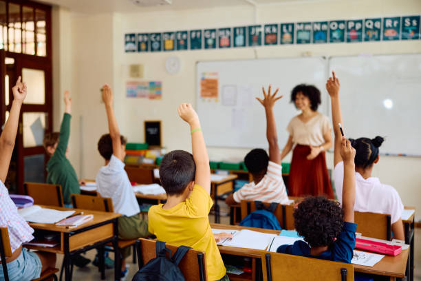 istock Elementary school children with hands raised in class to answer teacher's question 2202092155