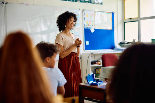 istock Elementary school teacher at front of class talking to children with hands clasped 2202092224