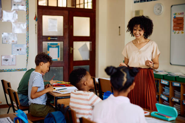 istock Cheerful elementary school teacher talking to children in classroom, smiling 2202092910