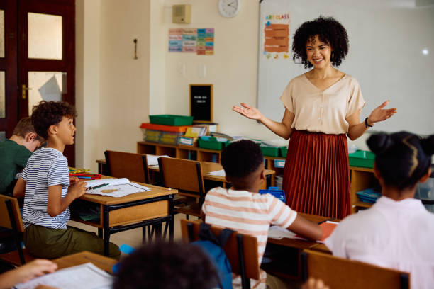 istock Cheerful elementary school teacher talking to children in classroom, smiling 2202092947
