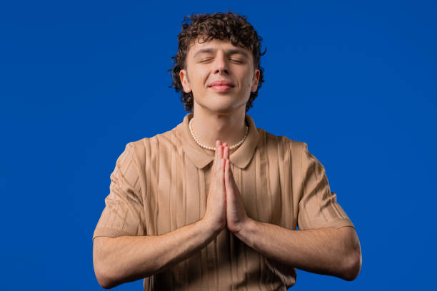istock Young curly haired man praying with crossed fingers on blue. Guy begs someone 2202093030