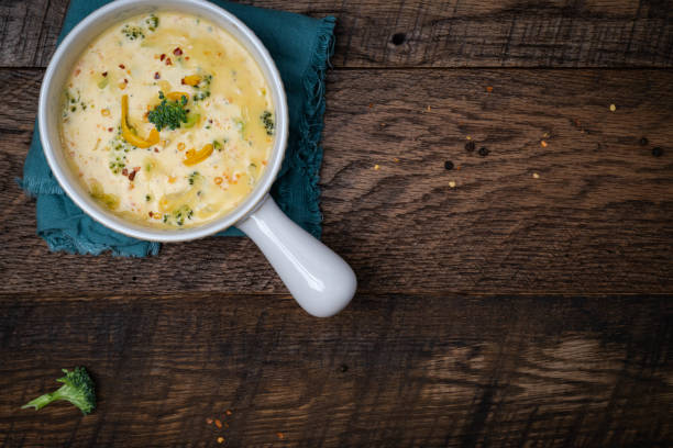 istock Creamy, Broccoli cheddar soup in white bowls with handle on a walnut table background with blue napkins. 2202093677