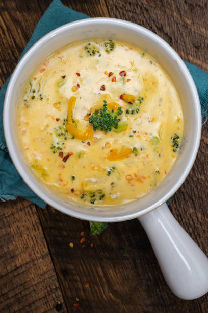 istock Creamy, Broccoli cheddar soup in white bowls with handle on a walnut table background with blue napkins. 2202093680