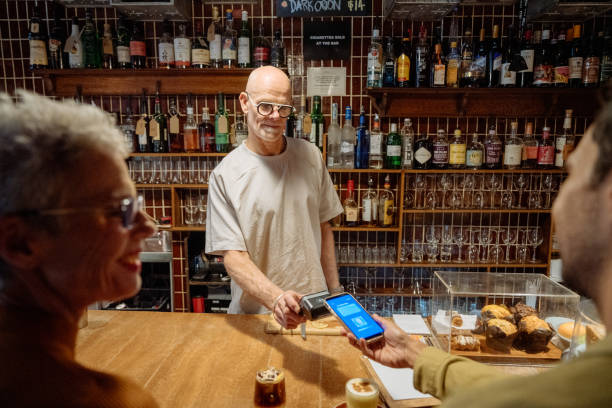 istock Mature barista working in cafe and serving customers. Customers paying by contactless method 2202096489