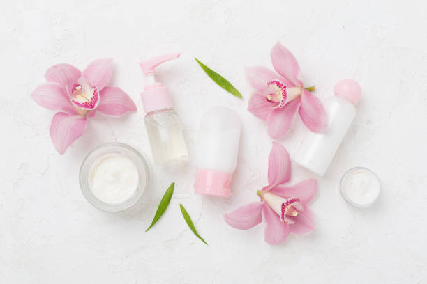 istock Bottles and jars with cream and orchids on color background, top view 2202101328