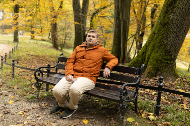 istock Young sad 30s man sitting alone on bench in autumn park. Thinking about life. Spending time alone in nature. Tired lost human guy wait, worship God 2202103818