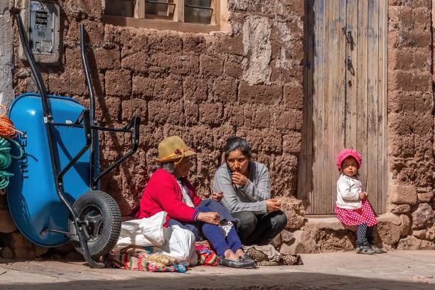 Pisac, Peru – February 23, 2020: Peruvian women and a child selling goods on Pisac streets by a rustic door