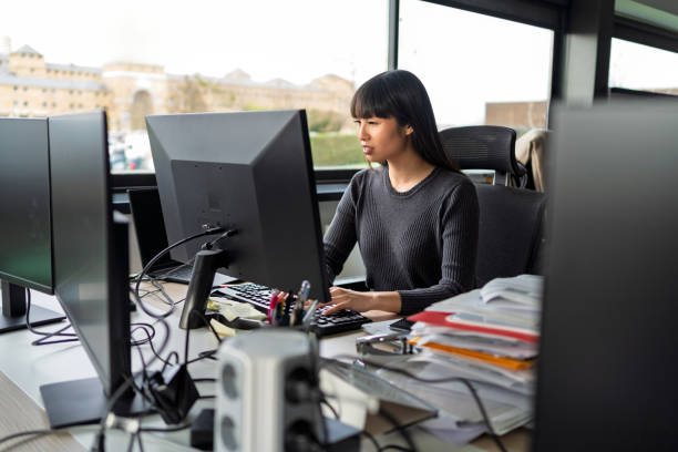 istock Focused businesswoman typing on a keyboard, working diligently on a computer in a bustling modern office filled with natural light 2202106801